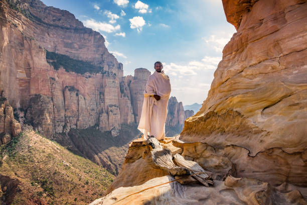 Monk stands in front of the Abuna Yemata Guh rock-hewn Christian church located in Gheralta Mountains,Hawzen, Tigray region, Ethiopia. The Gheralta cluster includes more than 30 rock-hewn churches dating from the middle ages.
